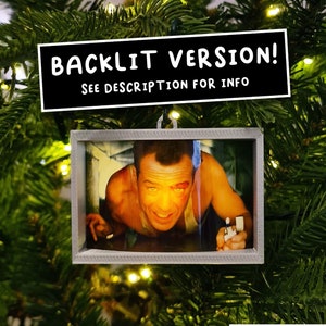 May include: A Christmas ornament featuring a framed image of a man with a black eye, looking up at the camera. The ornament is hanging on a green Christmas tree. The text "BACKLIT VERSION! SEE DESCRIPTION FOR INFO" is displayed above the ornament.