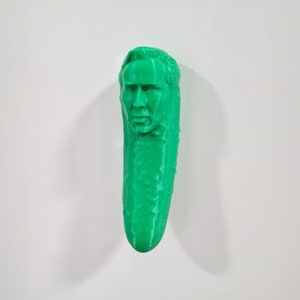 Puede incluir: Una escultura 3D impresa en verde de una cabeza humana sobre un pepino.