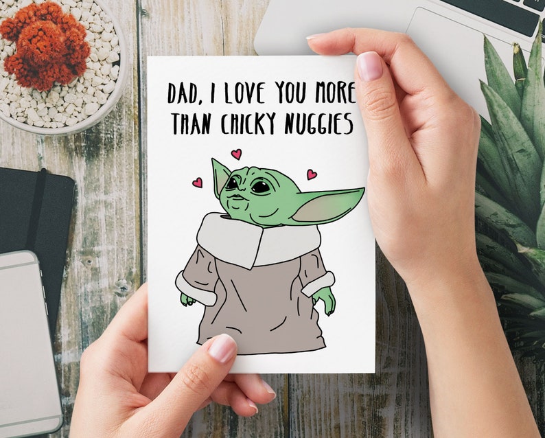 Puede incluir: Una tarjeta blanca con un personaje de dibujos animados verde con ojos grandes y un abrigo marr&oacute;n. La tarjeta dice "Pap&aacute;, te quiero m&aacute;s que a las nugguets de pollo".