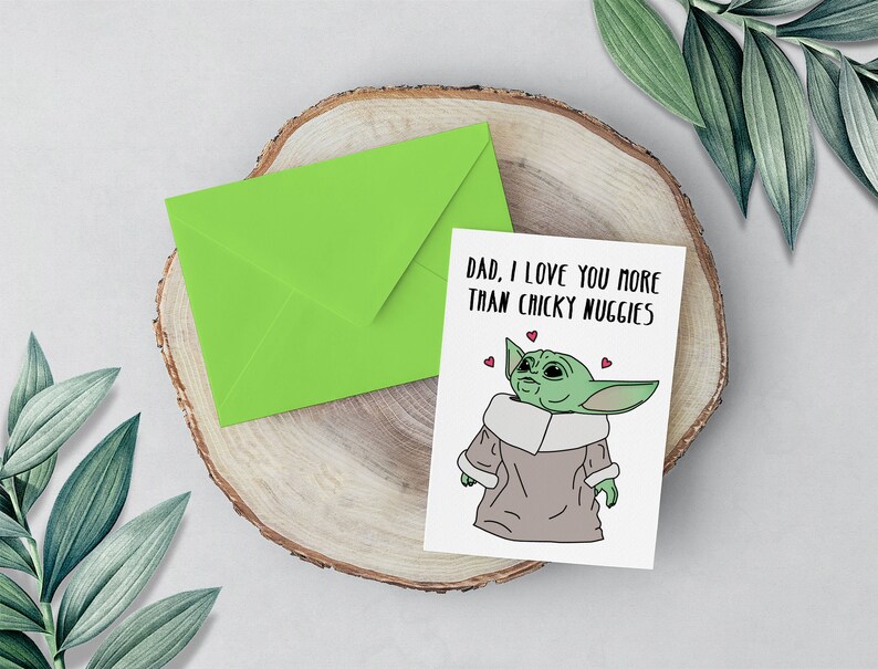 Puede incluir: Una tarjeta verde con un sobre blanco sobre una superficie de madera. La tarjeta presenta un personaje de dibujos animados con el texto "Pap&aacute;, te quiero m&aacute;s que las nugguets de pollo".