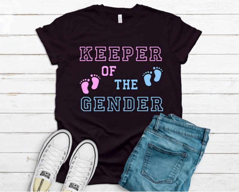 May include: Black t-shirt with the text "KEEPER OF THE GENDER" in white outlined letters. Pink and blue footprints are on either side of the word "THE".