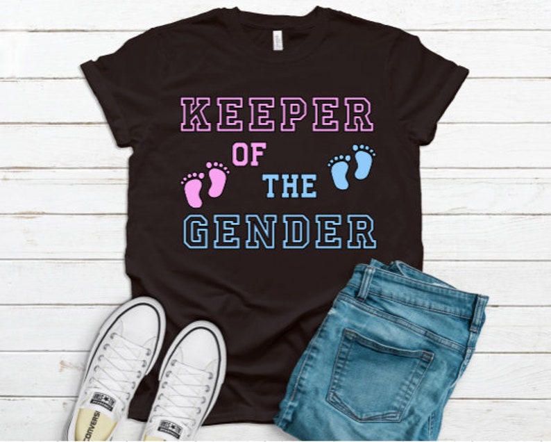 May include: Black t-shirt with the text "KEEPER OF THE GENDER" in white with blue and pink outlines. The text is surrounded by two footprints, one pink and one blue.