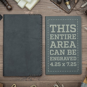 May include: Two dark gray leather journals with stitched edges. The journal on the right has the text "THIS ENTIRE AREA CAN BE ENGRAVED 4.25 x 7.25" printed on the front.