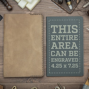 May include: Two brown leather journals with stitched edges. The journal on the right has the text "THIS ENTIRE AREA CAN BE ENGRAVED 4.25 x 7.25" printed on the front.