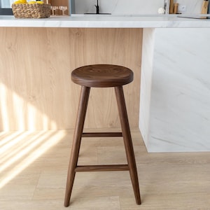 May include: A solid wood bar stool with a round seat and a simple design. The stool is made of dark brown wood and has a natural finish.