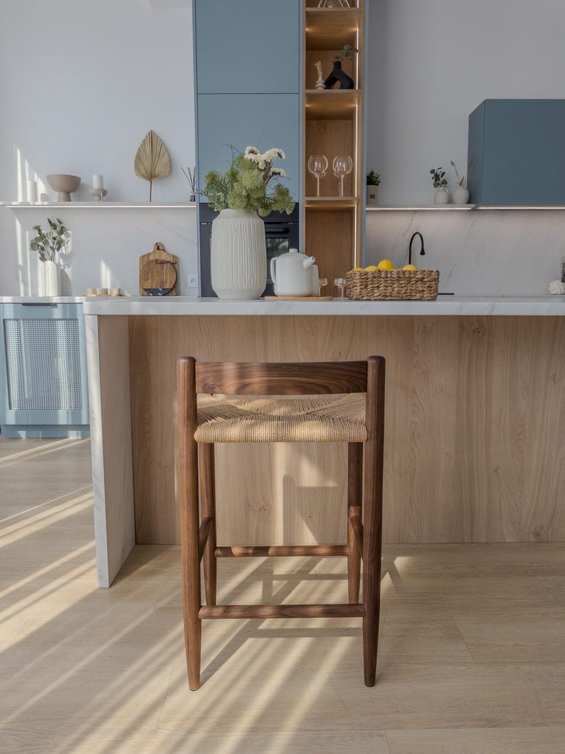 May include: A wooden bar stool with a woven cane seat. The stool is brown and has a natural finish. It is sitting on a light wood floor.