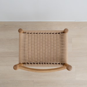 May include: Top view of a woven chair seat with a natural wood frame. The seat is made of a light brown woven material and the frame is made of a light brown wood.