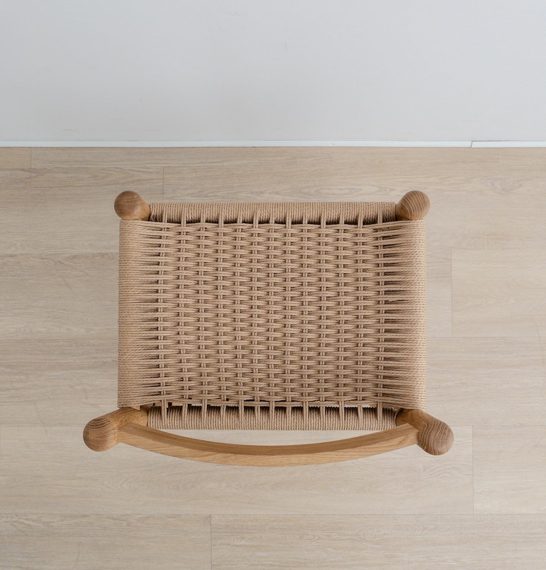 May include: Top view of a woven chair seat with a natural wood frame. The seat is made of a light brown woven material and the frame is made of a light brown wood.