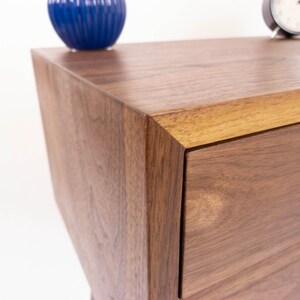 May include: A close-up of a wooden dresser with a drawer. The dresser is made of walnut wood and has a natural finish. The drawer is open and shows the wood grain.