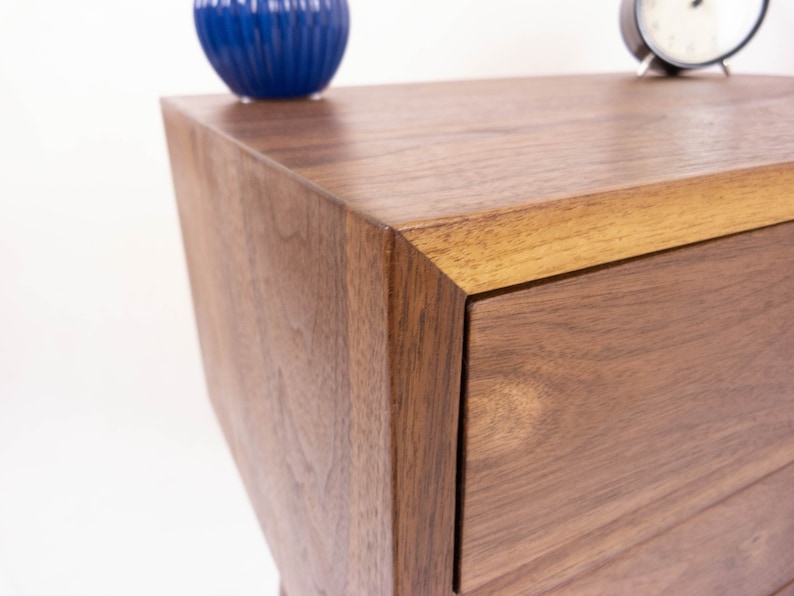 May include: A close-up of a wooden dresser with a drawer. The dresser is made of walnut wood and has a natural finish. The drawer is open and shows the wood grain.
