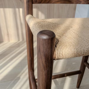 May include: A close-up of a wooden chair with a woven seat. The chair is made of dark wood and has a simple, modern design.