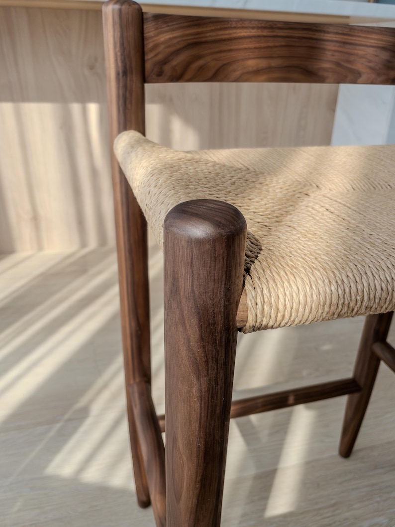 May include: A close-up of a wooden chair with a woven seat. The chair is made of dark wood and has a simple, modern design.