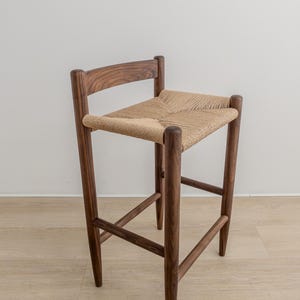 May include: A wooden stool with a woven seat. The stool is made of dark brown wood and has a simple, modern design.