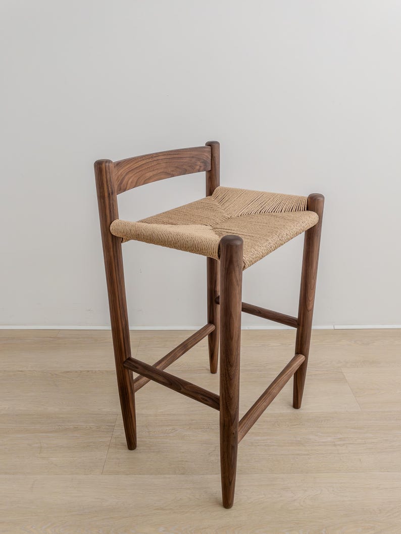May include: A wooden stool with a woven seat. The stool is made of dark brown wood and has a simple, modern design.