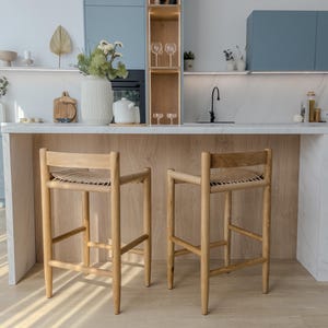 May include: Two wooden bar stools with woven seats in a modern kitchen with white countertops and blue cabinets.