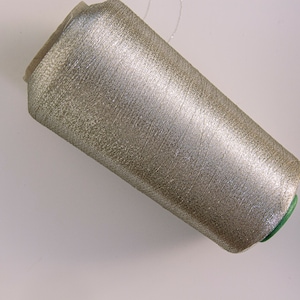 Puede incluir: Una bobina de hilo metálico plateado con una bobina de plástico verde.
