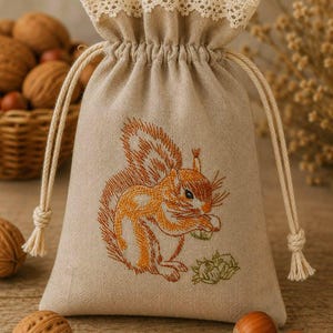 May include: A beige drawstring bag with a detailed embroidered squirrel design in shades of orange and brown. The bag has a lace trim at the top and a drawstring closure. The bag is filled with nuts.
