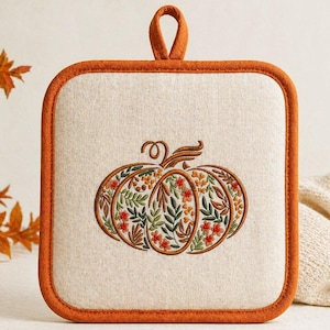 Puede incluir: Manopla cuadrada beige con un diseño de calabaza bordada. La calabaza está llena de patrones florales y de hojas en tonos naranja, verde y rojo. Tiene un borde naranja y un lazo para colgar.