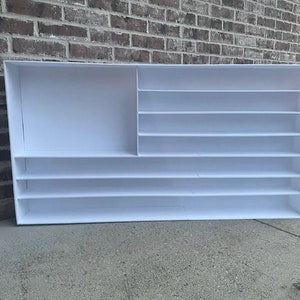 May include: White shelf unit with multiple shelves and a large open compartment. The shelf unit is made of a white material and has a simple design.