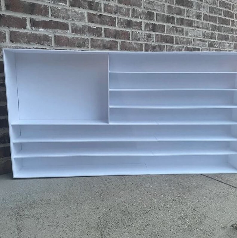 May include: White shelf unit with multiple shelves and a large open compartment. The shelf unit is made of a white material and has a simple design.