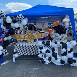 May include: A large white, black and gold balloon number "500" with a chequered tablecloth in the background. The number is made of balloons and is decorated with a graduation cap and a chequered pattern.