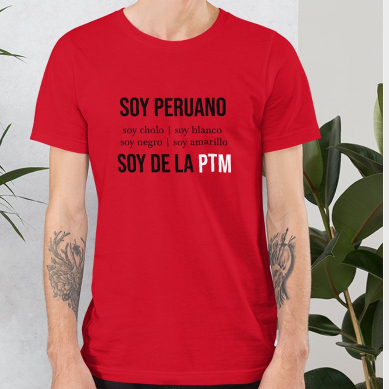 May include: Red t-shirt with black text that reads "SOY PERUANO soy cholo | soy blanco soy negro | soy amarillo SOY DE LA PTM"
