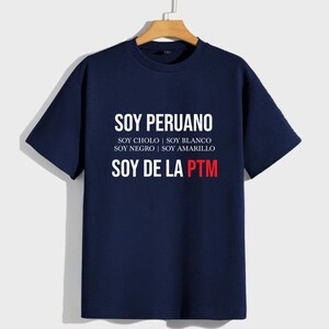 May include: A navy blue t-shirt with white text that reads "SOY PERUANO", "SOY CHOLO | SOY BLANCO", "SOY NEGRO | SOY AMARILLO", and "SOY DE LA PTM" in red.