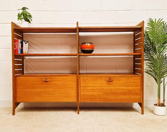 May include: A wooden shelving unit with two vertical sections, each featuring two open shelves and a lower cabinet with a drop-down door. The unit has slatted side supports, a light brown wood finish, and small wooden handles on the cabinet doors.