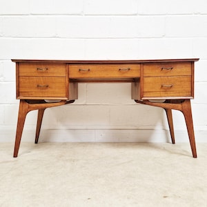 May include: A wooden desk featuring a rectangular top, a central drawer, and two stacks of two drawers on either side. The desk is supported by four tapered legs with structural supports connecting the legs to the drawer units, finished in a warm brown tone.