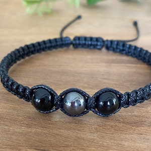 May include: A black braided bracelet with three beads. The beads are black, grey, and black.