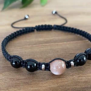 May include: A black cord bracelet with three black beads and one light brown bead. The bracelet has a sliding knot closure.