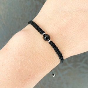 May include: A black braided bracelet with a black onyx bead and silver accents.