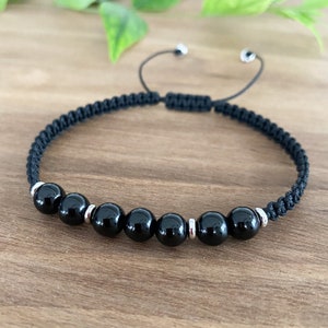 May include: Black onyx beaded bracelet with silver spacers on a black cord. The bracelet is adjustable with a sliding knot.