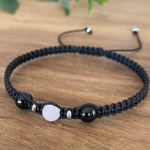 May include: Black braided bracelet with a pink and two black beads. The bracelet has a sliding knot closure.