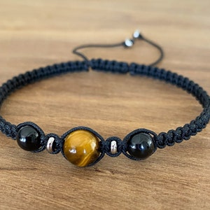May include: A black cord bracelet with three beads: two black onyx beads and one tiger's eye bead.