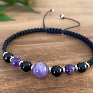 Może przedstawiać: Bransoletka z czarnego sznurka z koralikami z ametystu i czarnymi. Bransoletka ma zsuwany zamek z węzła.