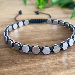 May include: A silver bracelet with hexagonal beads connected by black string.