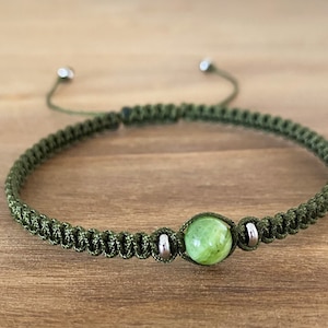 May include: A green braided bracelet with a green gemstone bead and silver metal accents.