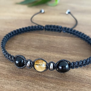 以下が含まれることがあります： 黒いコードのブレスレットに、黒オニキスビーズ2つと、金色シトリンビーズ1つがついたブレスレットです。