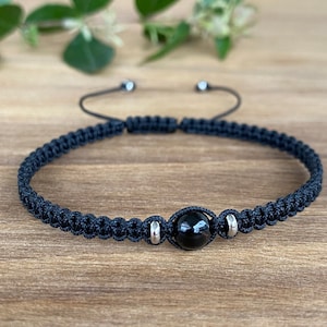 May include: Black braided bracelet with a black gemstone bead and silver accents.