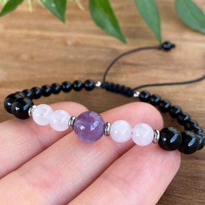 May include: A black, white and purple beaded bracelet with a sliding knot closure. The bracelet features black onyx, rose quartz and amethyst beads.