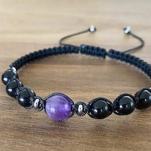 Może przedstawiać: Bransoletka z czarnego sznurka z czarnymi koralikami i jedną fioletową perłą ametystową.