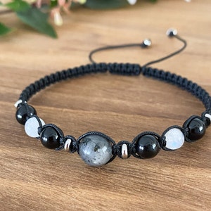 May include: A black cord bracelet with black, white, and gray gemstone beads. The bracelet has a sliding knot closure.