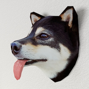 以下が含まれることがあります： 白い壁に、紙でできた黒と白の柴犬の頭が、舌を出して取り付けられています。