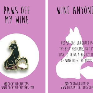 Puede incluir: Un pin de esmalte dorado con un gato negro sentado con una copa de vino. El texto "PAWS OFF MY WINE" est&aacute; por encima del gato. El texto "COCKTAILCRITTERS WWW.COCKTAILCRITTERS.COM" est&aacute; debajo del gato.