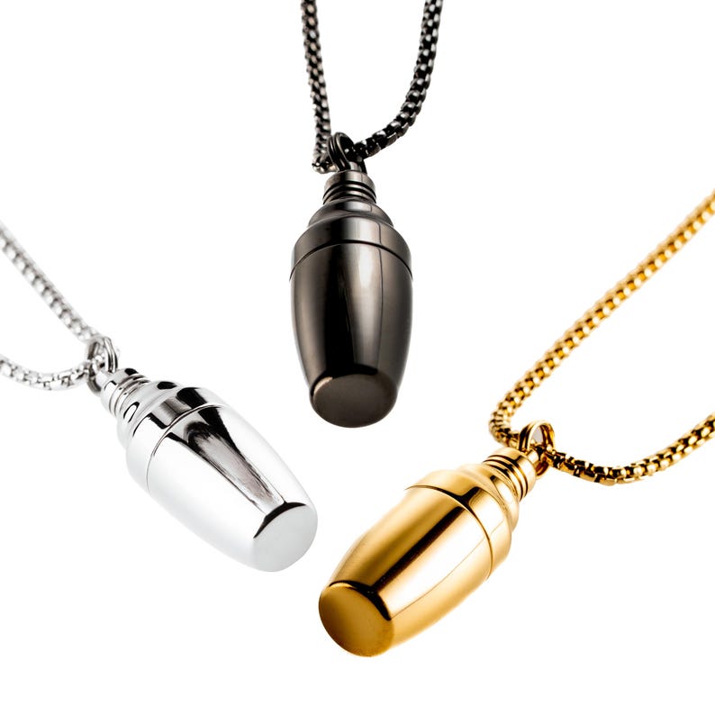 May include: Three pendant necklaces with a teardrop-shaped design. One is silver, one is black, and the other is gold. Each pendant hangs from a matching chain, creating a minimalist and elegant look.