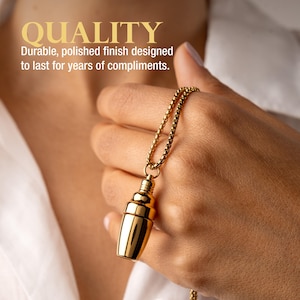 May include: A gold-colored necklace with a pendant shaped like a cocktail shaker. The pendant is suspended from a delicate chain. The image also includes the word "QUALITY" in gold lettering, with the text "Durable, polished finish designed to last for years of compliments."