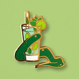 May include: Gold-tone enamel pin of a green snake holding a green and white cocktail glass with a lime wedge and a straw.