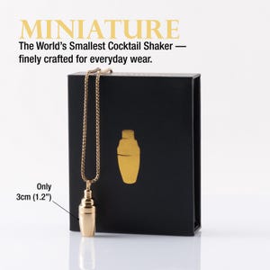 May include: A gold-colored miniature cocktail shaker pendant necklace, 1.2 inches in height, hangs in front of a black box. The box has gold text and a gold cocktail shaker graphic. The text reads "MINIATURE" and "The World's Smallest Cocktail Shaker - finely crafted for everyday wear."