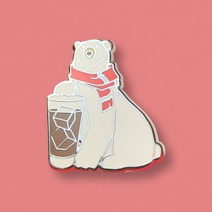 May include: A white polar bear wearing a red scarf holds a glass of iced coffee. The bear is sitting on a pink background.
